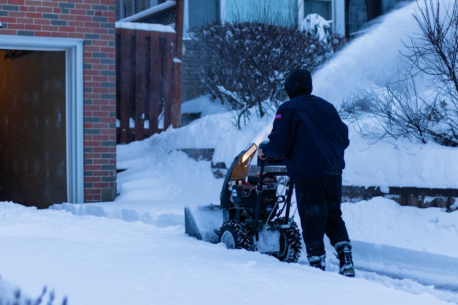 A snow-covered residential driveway being cleared with a snowblower