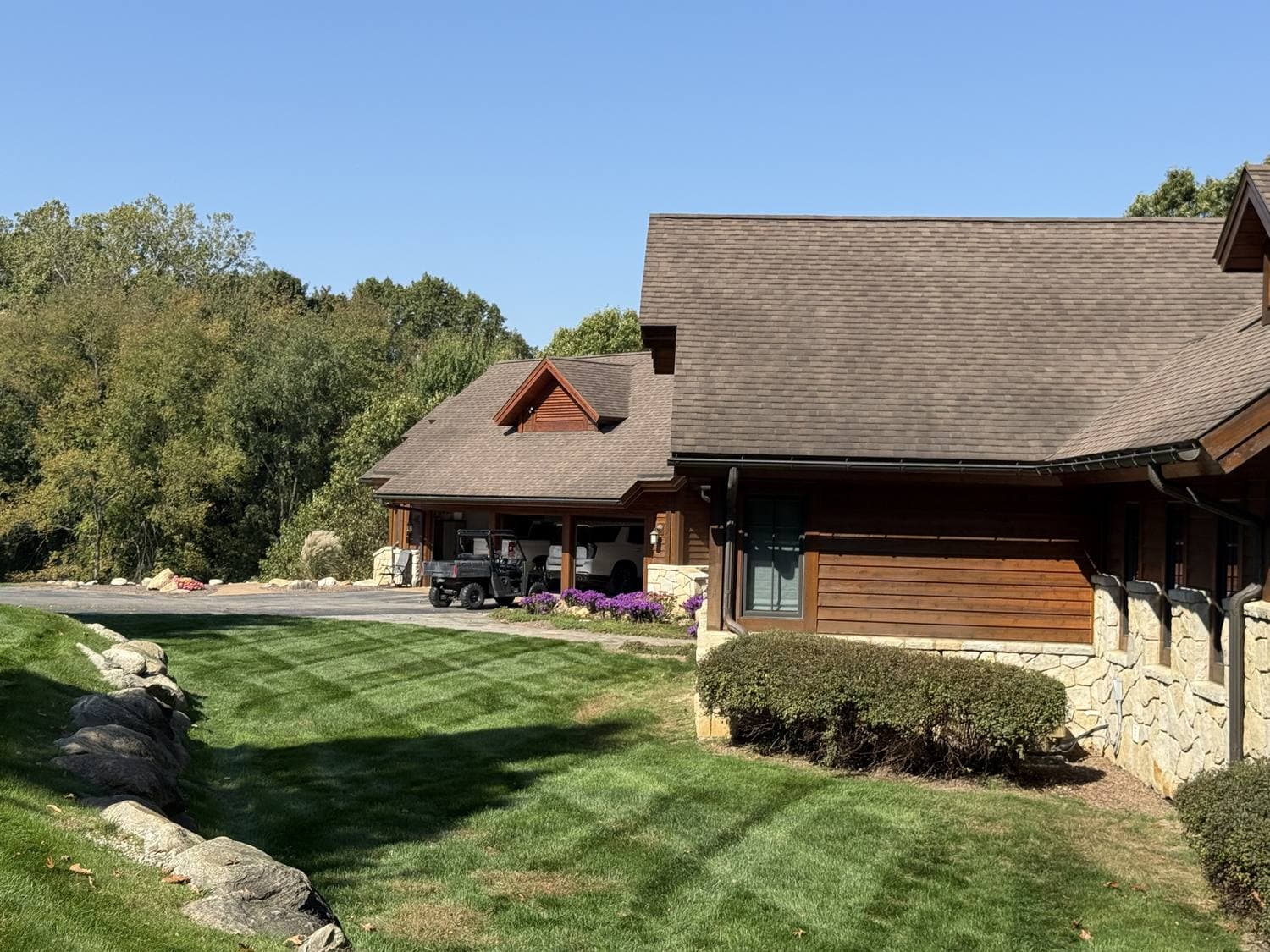 A striped lawn edged with a boulder-and-stone border at a wooded home